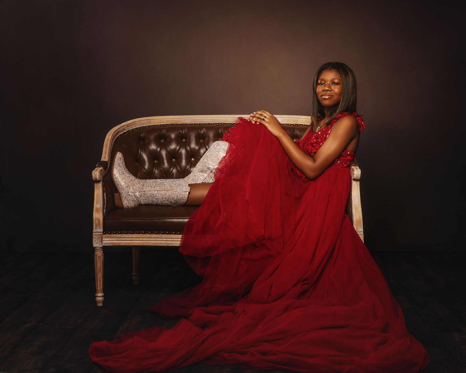 Studio portrait of Haley seated on a vintage settee in a red gown